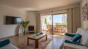 Een woonkamer met een bank, salontafel, televisie, open haard en uitzicht op het landschap.