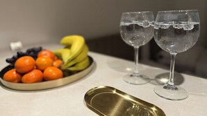 Ein Tisch mit einer Obstschale, gefüllt mit Orangen, Bananen und Trauben, sowie zwei Gläsern Wasser.