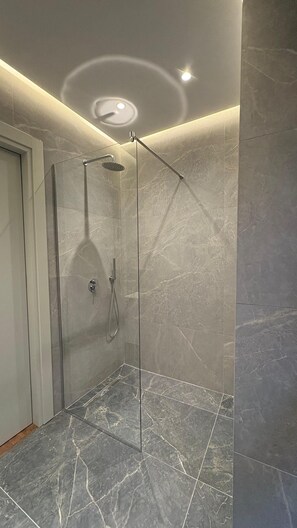 A modern bathroom with a glass-enclosed shower, marble flooring, and a recessed ceiling light.