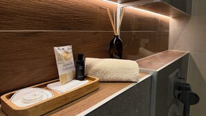 A bathroom vanity with a wooden tray holding a towel, a bottle of shower gel, and a small package.