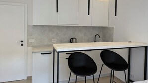 A modern kitchen with white cabinets, a black countertop, and two black chairs.