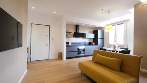 Un appartement moderne doté d’un salon avec un canapé jaune, d’une cuisine avec des meubles sombres et d’un coin repas comprenant une table et des chaises.