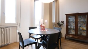 Un coin repas avec une table ronde, des chaises noires, une lampe suspendue jaune, un radiateur et un meuble avec des portes en verre.
