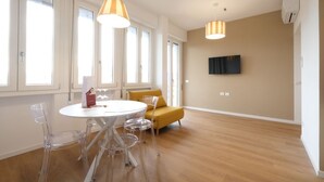 Un salon moderne avec une table ronde, des chaises transparentes, un canapé jaune et un téléviseur fixé au mur.