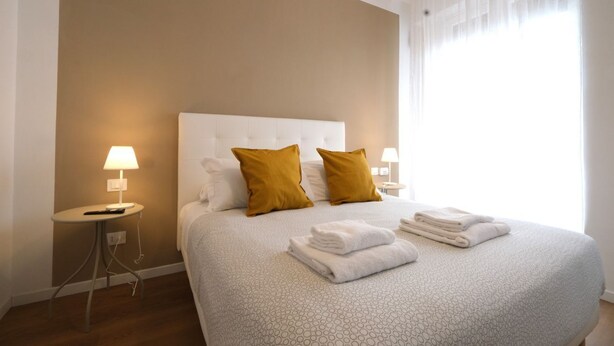 Une chambre d’hôtel avec un grand lit, deux oreillers, une table de chevet avec une lampe et une fenêtre avec des rideaux.