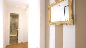 Un couloir doté d’un plancher en bois, une porte blanche donnant sur une salle de bain et un grand miroir décoratif accroché au mur.