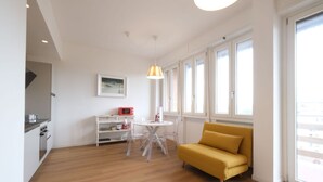 Un salon moderne avec un plancher en bois, un canapé jaune, une table à manger avec des chaises et un coin cuisine équipé d’un four à micro-ondes.
