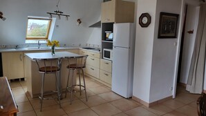 Una cuina amb una illa central, dos tamborets d'esbarjo, un refrigerador, un microones i una finestra amb vista a cases.