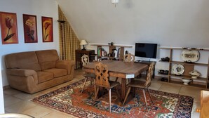 Un saló amb un sofà marró, taula de dinar de fusta i cadires, televisió, prestatges i plats decoratius.