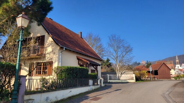 Una casa de dues plantes amb teulada de rajola vermella, un balcó i un pati tancat.