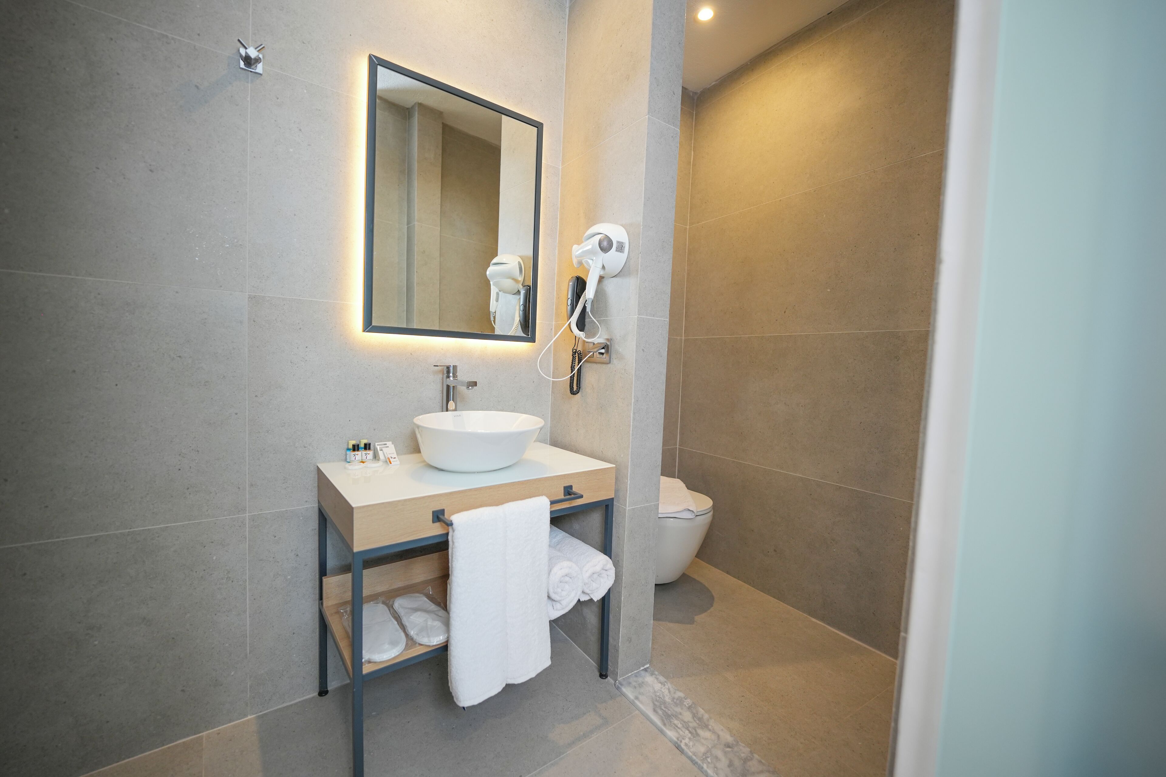 A modern bathroom with a large mirror, a sink, a towel rack, and a toilet.
