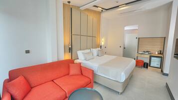 A modern hotel room with a large bed, a red sofa, a small round table, and a desk with a computer.