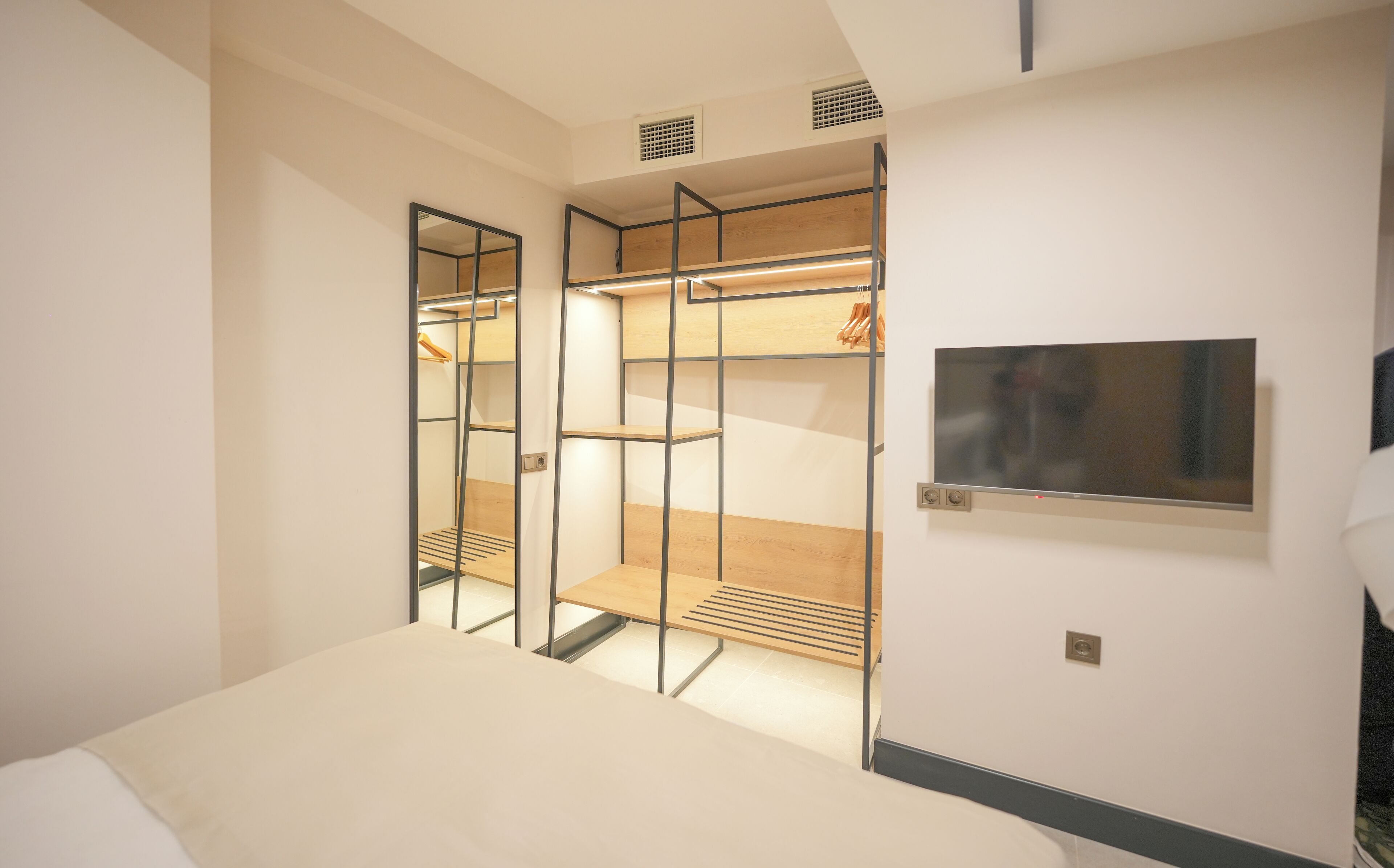 A modern bedroom with a bed, a walk-in closet with shelves, and a TV mounted on the wall.