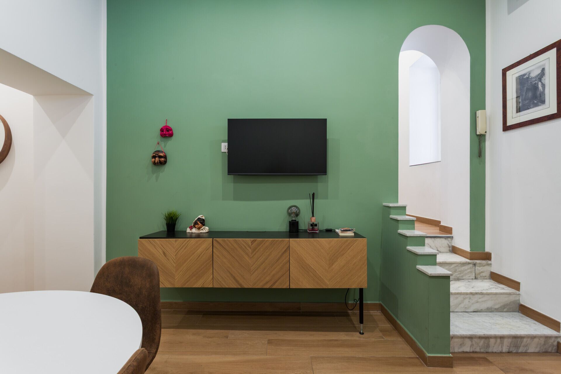 Ein modernes Wohnzimmer mit grüner Wand, einem Holzkasten, einem Flachbildfernseher und einer Treppe mit Marmorstufen.