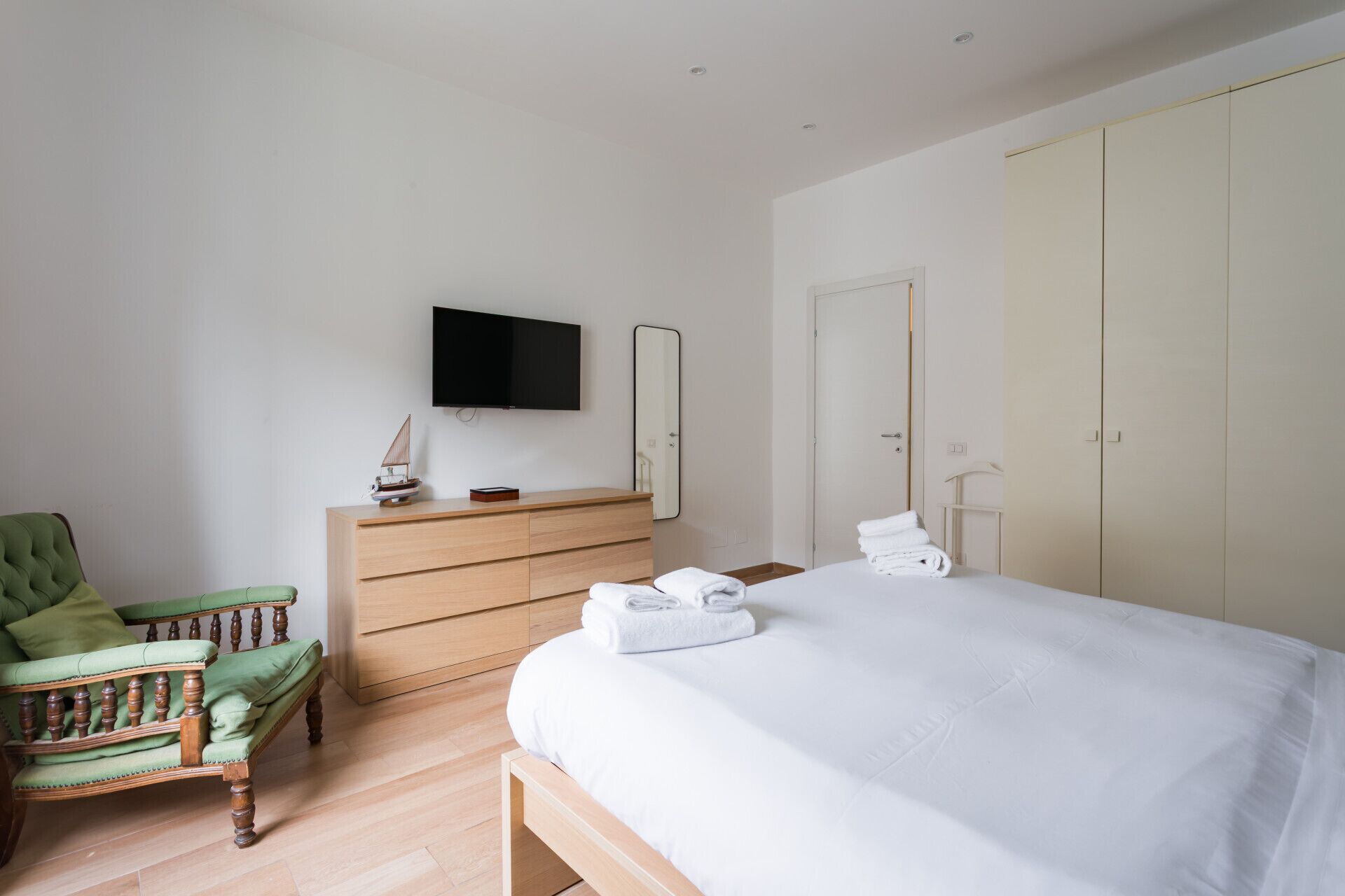 Ein Hotelzimmer mit einem Bett, einem Holzschrank, einem grünen Sessel, einem Fernseher und einem Kleiderschrank.