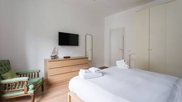 Ein Hotelzimmer mit einem Bett, einem Holzschrank, einem grünen Sessel, einem Fernseher und einem Kleiderschrank.