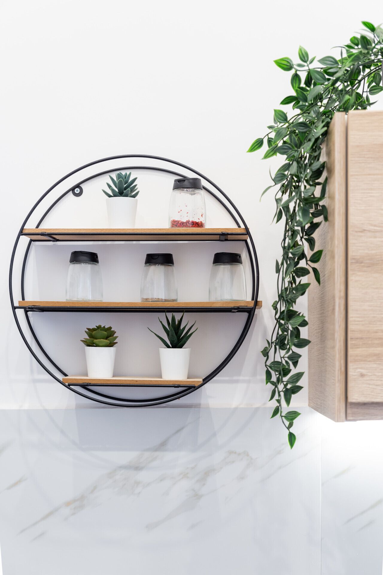 A circular metal shelf with three wooden shelves, each holding a potted plant and a glass jar with a black lid.