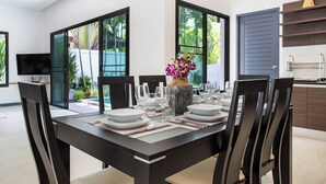 A modern dining area with a large table set for four, surrounded by dark chairs. - Villa Elima, lovely pool two bedrooms villa at rawai (rawai)
