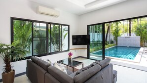 A modern living room with a large window, a flat-screen TV, a pool, and a potted plant. - Villa Elima, lovely pool two bedrooms villa at rawai (rawai)