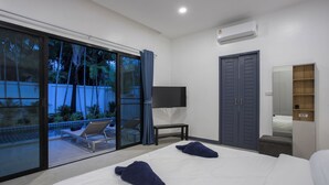 A modern hotel room with a large bed, a TV, a wardrobe, and a balcony with a view of palm trees. - Villa Elima, lovely pool two bedrooms villa at rawai (rawai)