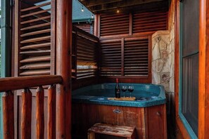 A wooden spa area with a hot tub, wooden slats, and a stone wall. - Spacious 4BR Cabin Retreat w/ 2 Game Rooms, Double Wraparound Decks & Views (Pigeon Forge)