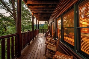 A wooden deck with chairs and a railing, overlooking a forested area.