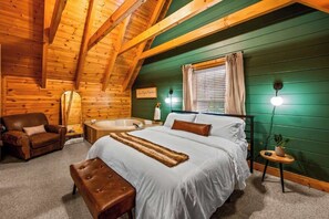 A cozy log cabin bedroom with a large bed, a wooden bench, a chair, a bathtub, and a small table with a plant. - Spacious 4BR Cabin Retreat w/ 2 Game Rooms, Double Wraparound Decks & Views (Pigeon Forge)