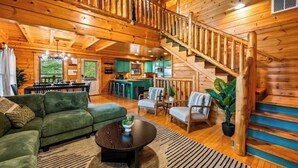 A spacious wooden cabin with a living area, kitchen, and a staircase.
