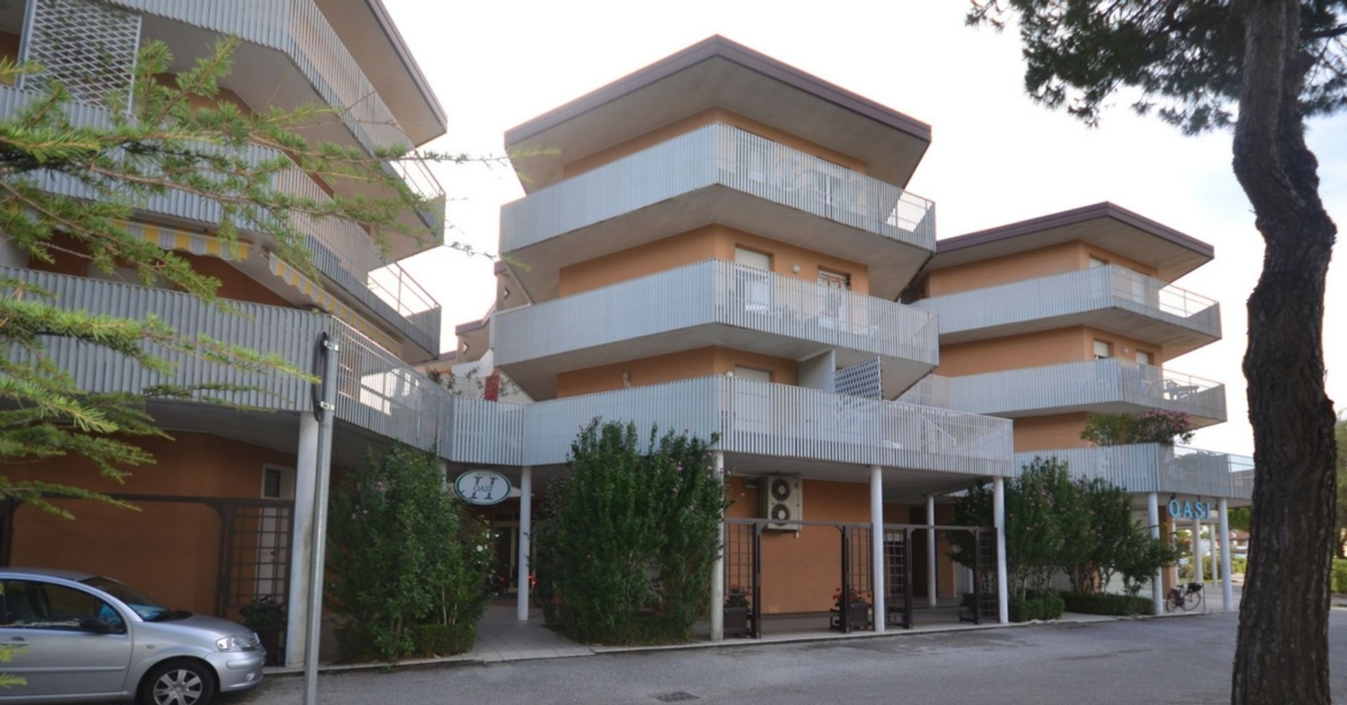 A multi-story building with balconies and a car parked in front.
