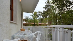 A balcony with a table set for two, white chairs, and a wicker basket. - Peaceful apartment in a leafy setting (Lignano Sabbiadoro)