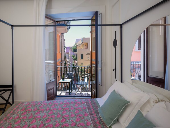A bedroom with a balcony, a bed with patterned bedding, and a view of the cityscape.