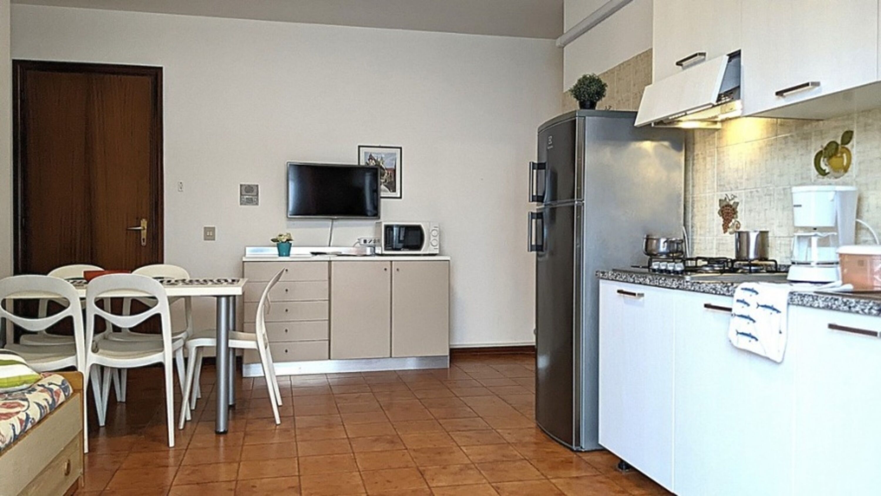 Una cucina compatta con zona pranzo, TV e frigorifero.