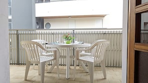 A round table with four chairs, a potted plant, and a glass of water on a balcony with a white railing.