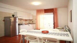 A compact kitchen with a refrigerator, stove, and dining table with chairs. - Apartment near the beach and Lignano’s attractions (Lignano Sabbiadoro)