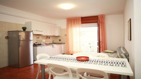 A compact kitchen with a refrigerator, stove, and dining table with chairs.