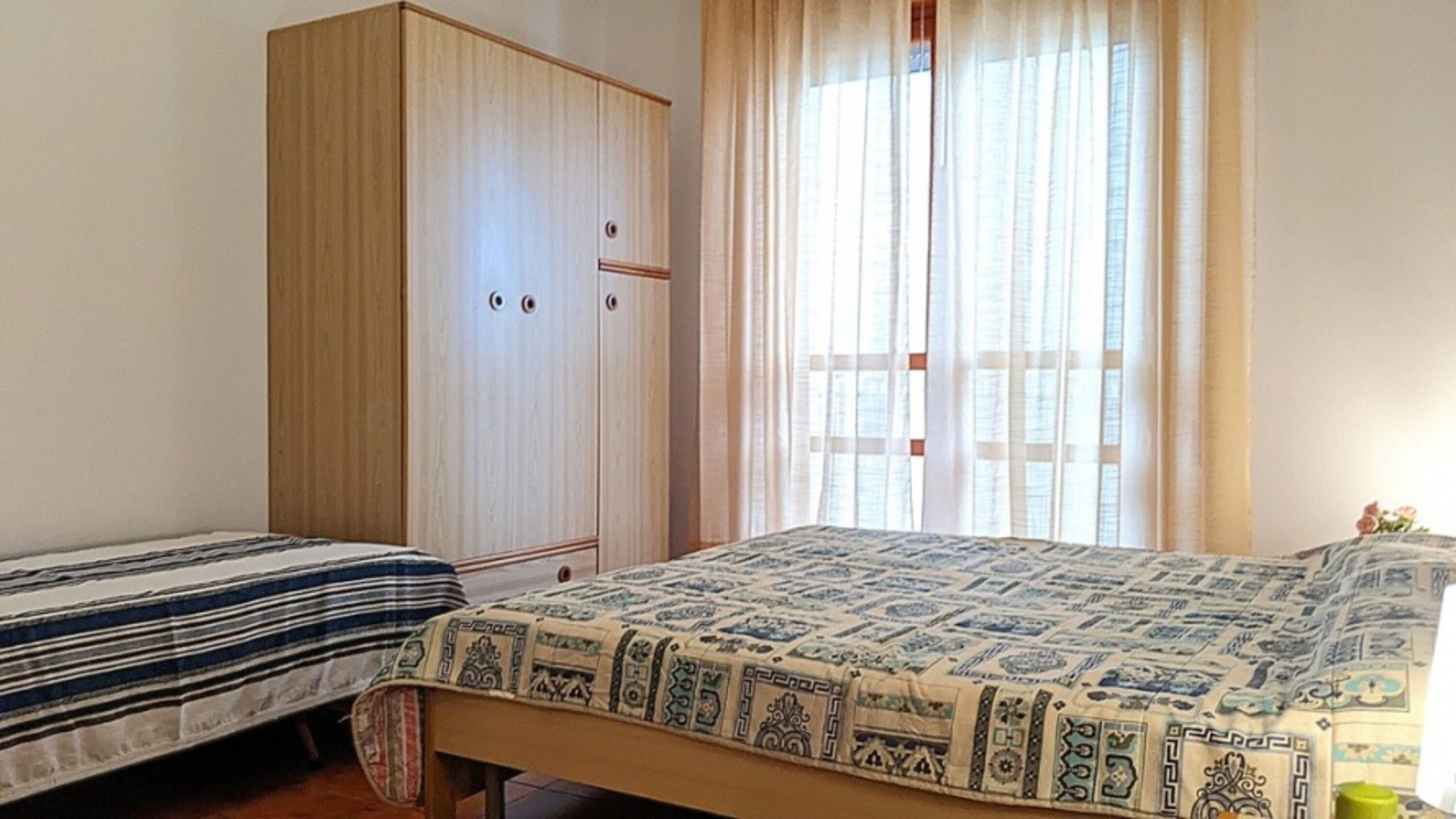 A bedroom with two beds, a wardrobe, and a window with curtains.