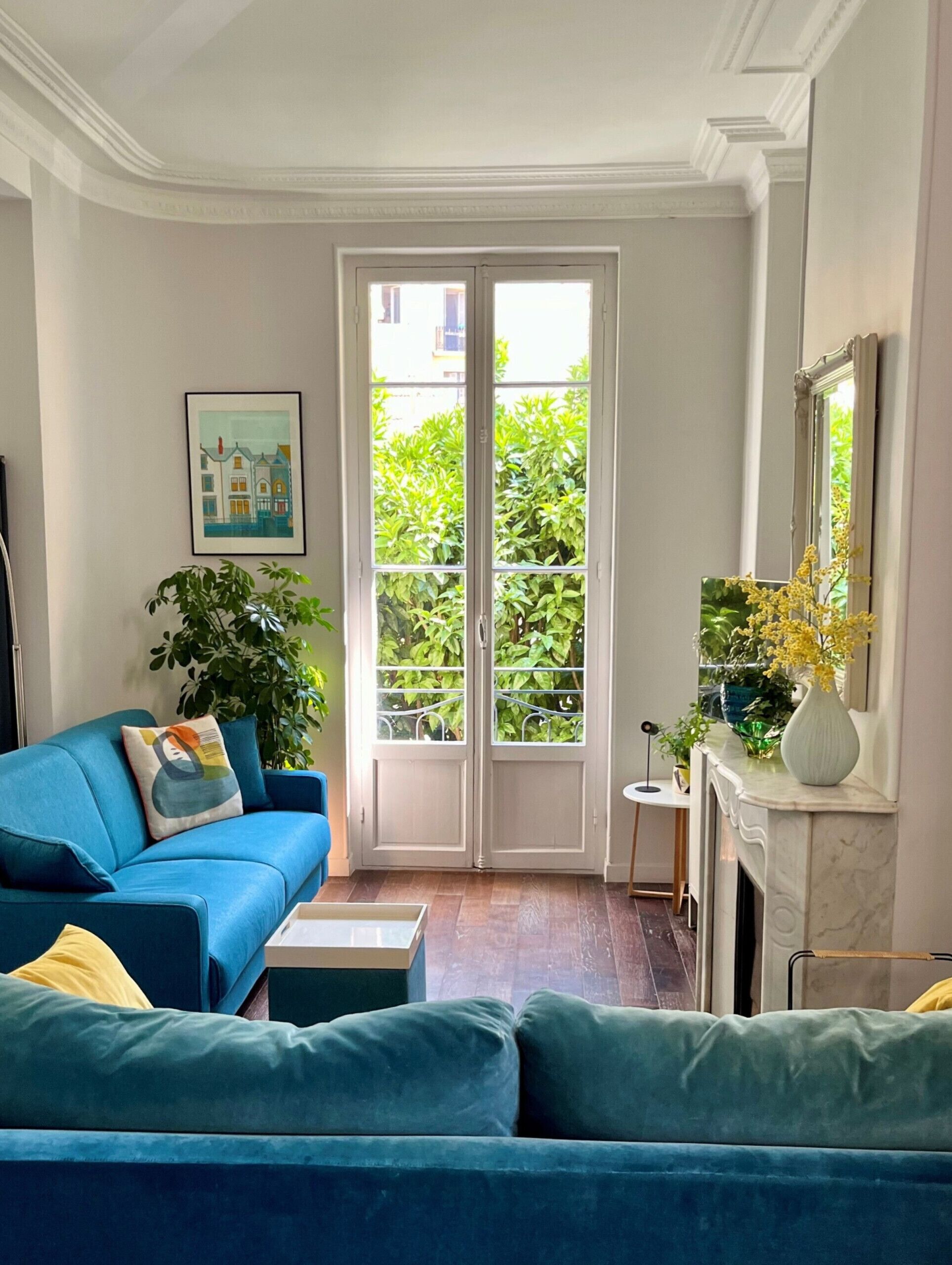 A living room with a blue sofa, a small table, a fireplace, and a large window with a view of greenery.