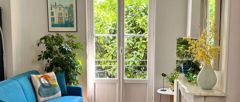 A living room with a blue sofa, a small table, a fireplace, and a large window with a view of greenery.
