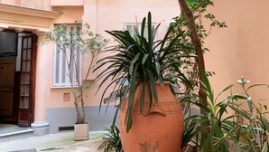 A courtyard with a large terracotta pot, potted plants, and a building with a beige facade and shutters. - Berlioz Blue AP4458 by Riviera Holiday Homes (Niza)