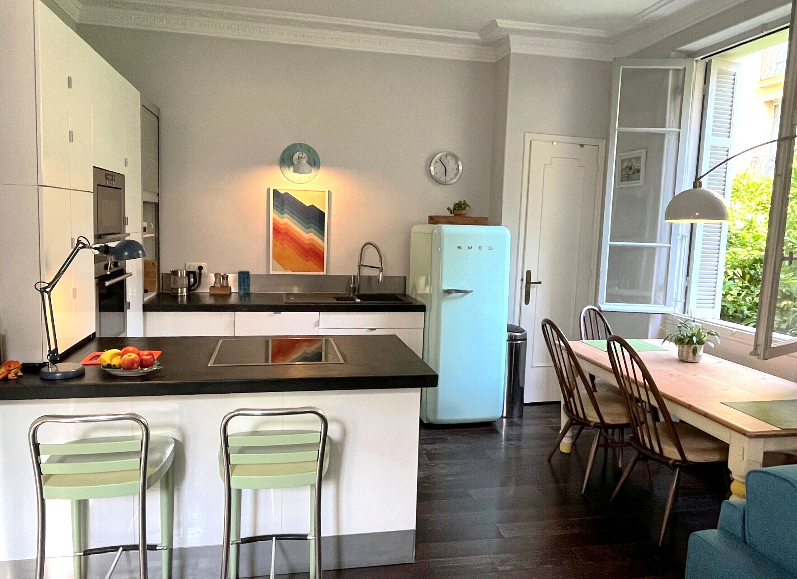 Cozinha moderna com ilha central, área de jantar com mesa e cadeiras, e vista pela janela.