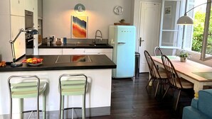 A modern kitchen with a central island, a dining area with a table and chairs, and a view through a window. - Berlioz Blue AP4458 by Riviera Holiday Homes (Niza)