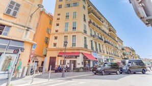 Un immeuble à plusieurs étages, doté d’un auvent rouge, d’un café et d’un fourgon stationné.