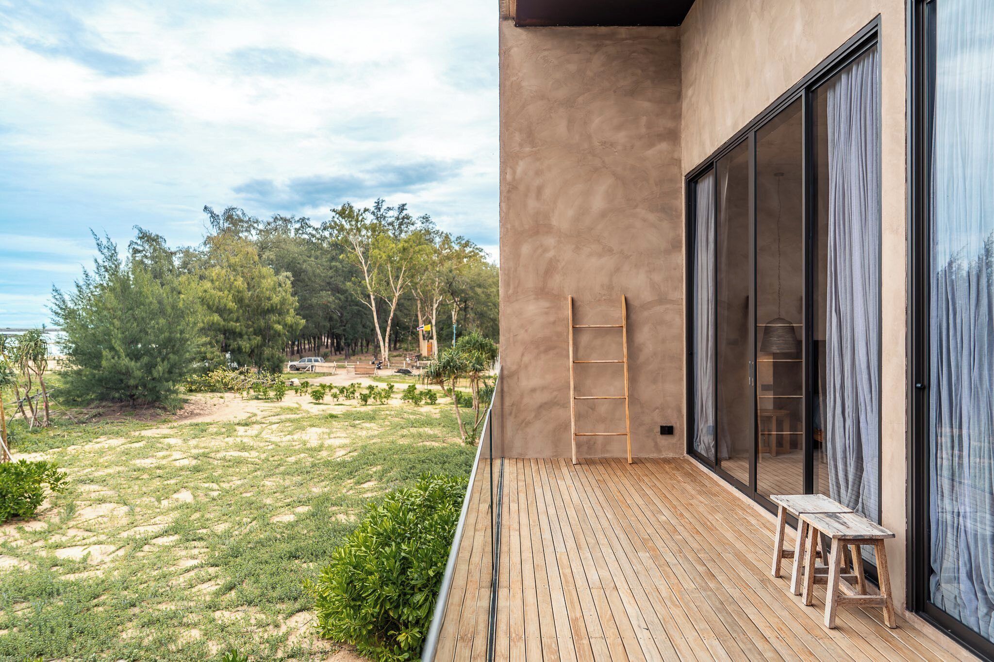 A wooden deck with a bench and a ladder, leading to a glass door with curtains.