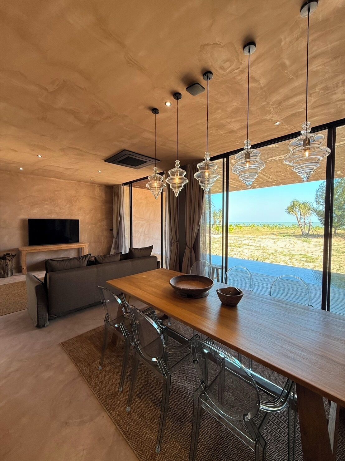 A modern dining area with a wooden table, clear chairs, and hanging crystal chandeliers.