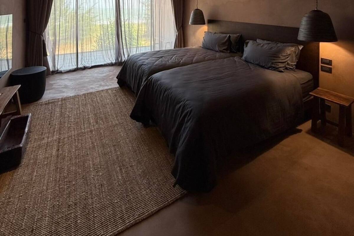 Une chambre moderne avec un grand lit, un bureau et une vue sur l’extérieur à travers des rideaux légers.