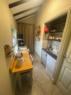 Une cuisine compacte avec une table en bois, un appareil électroménager noir, un lave-vaisselle blanc et un pare-éclaboussures carrelé.