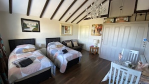 A room with two beds, a wooden ceiling, a chandelier, and a white door.