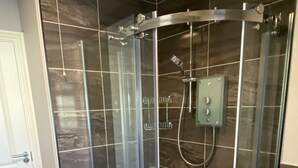 A glass-enclosed shower stall with a control panel, a door, and a tiled floor.