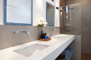 A modern bathroom with two sinks, a shower, and a large mirror.