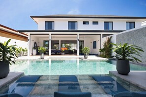 A modern house with a swimming pool, outdoor seating, and potted plants.